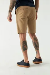 Bermuda de gabardina color beige, corte chino, con bolsillos laterales y traseros, cierre con cremallera y botón, presillas para cinturón y logo bordado.