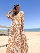 Vestido largo de corte amplio con estampado floral en tonos beige y blanco. Tiene escote en V con lazos y mangas largas abullonadas.