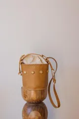 Cartera tipo canasta color terracota con textura símil piel de cocodrilo, con forro de tela blanca ajustable con cordón. Tiene correa larga de cuero marrón con hebilla dorada.
