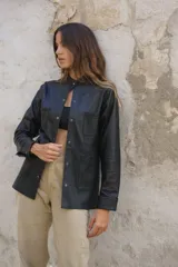 Camisa negra de cuero ovino con cuello mao, cierre frontal con botones a presión, dos bolsillos de parche en el pecho y tachas doradas en cuello, bolsillos y puños.