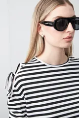 Remera de manga larga a rayas horizontales blancas y negras, con escote redondo y aberturas en los hombros sujetas con lazos regulables de tela a rayas.