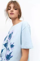 Remera lila de algodón con estampado de flores en tonos naranja y rosa.