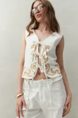 Chaleco blanco de algodón con bordados de cadenas doradas y lazos frontales.