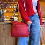Bandolera roja de cuero sintético con correa larga regulable combinada a tono. Tiene dos bolsillos frontales con cierre, apertura superior con cierre, división interna, bolsillos internos y bolsillo trasero con cierre.