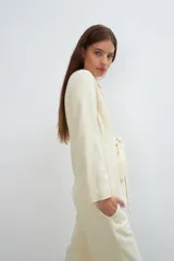 Chaqueta corta entallada color beige, con escote en V, manga larga, cierre frontal con lazo fijo y bolsillos escondidos. Confeccionada en lana fina sin teñir, diseñada exclusivamente por Don Baez.