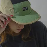 Gorra de visera estilo five-panel, color verde con visera beige y detalle de logo Pulau en el frente.
