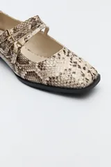 Zapato tipo Mary Jane color negro con textura de reptil, de charol sintético con punta cuadrada y triple tira con hebillas.
