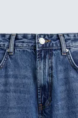 Pantalón de jean celeste de corte flare, con tiro medio, cinco bolsillos, cierre frontal con cremallera y botón, y bajo con acabado irregular.