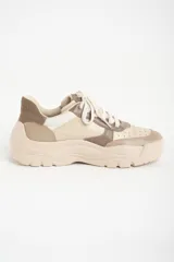 Zapatilla urbana de mujer con plataforma gruesa, combinando paneles de cuero en tonos beige, blanco roto y marrón topo. Presenta cordones anchos y un detalle de texto en el talón.