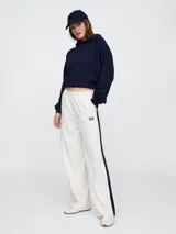 Pantalón deportivo blanco de corte ancho, con cintura elástica, cordón ajustable y raya lateral azul marino.