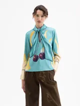 Camisa de manga larga color celeste con estampado de lunas amarillas y cerezas rojas. Presenta cuello con lazo anudado y ribetes en azul marino en el cuello, puños y cartera frontal.