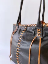Bolso tipo tote de cuero negro con costuras a la vista en color camel. Tiene doble asa de hombro y está forrada en tela.