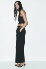 Pantalón marrón de tiro alto con cinturón negro, bolsillos delanteros y cierre frontal con cremallera y gancho metálico.