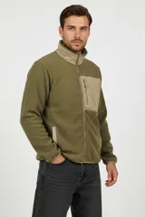 Campera de poliéster color verde militar con cuello alto y cierre frontal. Presenta un bolsillo con cierre en el pecho y dos bolsillos laterales, todos en color beige.