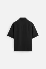 Camisa negra de corte relaxed fit, confeccionada en tejido con mezcla de modal. Tiene cuello bowling, manga corta, bolsillo de parche en el pecho y cierre frontal con botones.