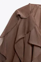 Blusa marrón de gasa con escote en V y manga larga abullonada. Presenta volantes en el mismo tejido y cierre frontal con botones.