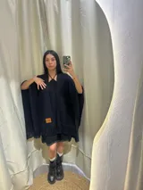 Ruana negra de lana merino uruguaya, tejida artesanalmente en telar. Tiene flecos en el borde inferior y etiqueta de cuero con logo de la marca.