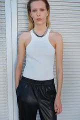 Pantalón jogger negro de corte amplio, confeccionado en tejido revestido tipo cuero sintético, con cintura elástica fruncida, bolsillos laterales y bajos deshilachados.