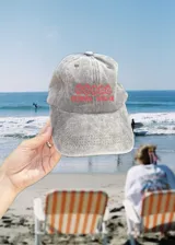 Gorro de visera de tela tipo denim o algodón lavado, color gris claro, con bordado frontal en hilo rojo que dice "COSTA DULCE" y un diseño abstracto arriba.