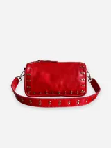 Bandolera marrón de cuero con tachas plateadas y correa de cuero con tachas plateadas. Tiene dos asas desmontables, una corta con tachas para llevarla en la mano o al hombro y una larga para llevarla al hombro o cruzada.