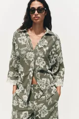 Camisa verde militar con bordado floral blanco, cuello solapa, escote en pico, manga tres cuartos con detalle de guipur y cierre frontal con botones.