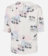 Blusa de viscolino color crudo con estampado de paisaje con palmeras y casas en tonos pastel. Tiene cuello redondo y mangas cortas abullonadas.