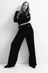 Pantalón negro de corte ancho, tiro alto, con bolsillos traseros decorativos con botón dorado y pliegues delanteros.