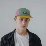 Gorra de cinco paneles con visera plana, color negro con secciones en verde y fucsia.