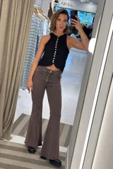 Top sin mangas color beige, con escote en V y cierre frontal de botones de nácar. Presenta costuras decorativas en el borde del escote y sisas.