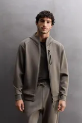 Sudadera con capucha color marrón topo, de corte regular fit, confeccionada en tejido técnico compacto de algodón con elasticidad. Cuenta con cuello subido, manga larga con bolsillo, bolsillos frontales con cierre de cremallera y acabados con rib del mismo tejido.