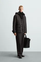 Parka negra de tejido técnico acolchado, corte regular fit, cuello alto con capucha ajustable, manga larga con puños ajustables, bolsillos de solapa en la cadera y bolsillo interior. Cierre frontal con cremallera oculta y botones a presión.