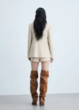 Chaqueta color beige con cuello de solapa, cierre frontal con botones, cuatro bolsillos frontales con solapa y manga larga.