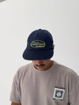 Gorro tipo gorra de béisbol color azul marino, con visera curva y bordado frontal en amarillo con la palabra "Sunrise" y "Sunset Flower".