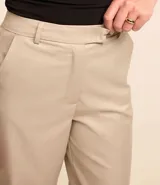 Pantalón de vestir color beige, de corte recto, con trabillas, cintura cruzada y cierre tradicional.