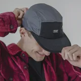 Gorra de cinco paneles gris y negro con logo de la marca Pulau en el frente.