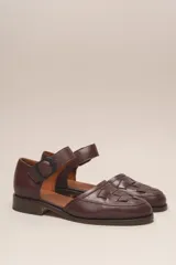Zapato marrón de cuero vacuno trenzado a mano, con correa al tobillo con hebilla negra y suela de cuero.