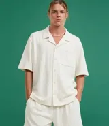Camisa de jacquard color crema, de corte oversized, con cuello solapa, manga corta, abotonadura frontal, bolsillo en el pecho y textura en relieve.