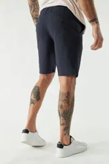 Bermuda color beige, de corte chino clásico, con bolsillos laterales y traseros, cierre con botón y cremallera, presillas para cinturón y logo bordado. Confeccionada en algodón y spandex.