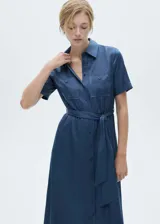 Vestido camisero midi color beige, de tela satinada, con cuello camisero, mangas cortas, dos bolsillos de parche en el pecho, lazo ajustable en la cintura y cierre frontal con botones.