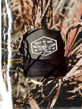 Gorra trucker negra con parche bordado en el frente con el logo de la marca Rest & Rise en color blanco.