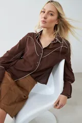 Camisa de vestir marrón con cuello clásico, cierre frontal con botones, mangas largas con puños abotonados y detalles de pespuntes blancos en cuello, solapa y canesú.