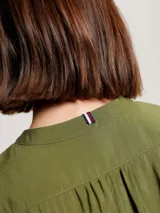 Camisa verde oliva de corte cropped, sin cuello, con cierre frontal de botones y mangas largas abullonadas con puños abotonados.