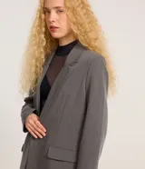 Blazer gris de sastrería, corte oversized, con cuello con solapas, manga larga y bolsillos frontales.