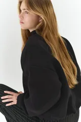 Campera negra de felpa con efecto neopreno, corte oversized y hombros caídos. Presenta cuello redondo, cierre frontal metálico, bolsillos delanteros insertados y elástico revestido en puños y bajo.
