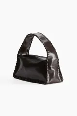 Cartera pequeña color marrón oscuro, de tejido revestido con tira entrelazada en los bordes. Tiene cierre superior, correa corta y forro de tafeta.