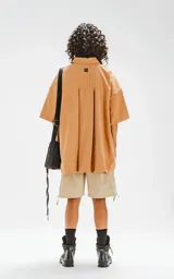 Camisa manga corta color beige, con cuello clásico, cierre frontal con botones, doble bolsillo con ojal en el delantero y silueta oversize.