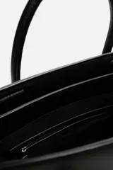 Bolso bandolera negro con detalle de cinturón, compartimento principal con cierre mediante doble imán, bolsillo interior con cierre mediante cremallera, dos asas de mano y un asa de hombro ajustable y extraíble.