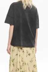 Camiseta de algodón color negro con efecto gastado (acid wash) y cuello redondo. Presenta un pequeño estampado en relieve color rosado en el pecho.