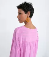 Blusa tipo blusón color rosado, de viscosa, con cuello redondo, manga larga acampanada, pliegues en los hombros, detalle de entredós en el escote y tiras de ajuste con borla.