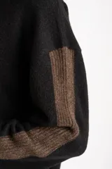Sweater negro de tejido grueso con cuello alto acanalado. Presenta una franja decorativa en las mangas y el cuello en hilo marrón con brillo (lurex).